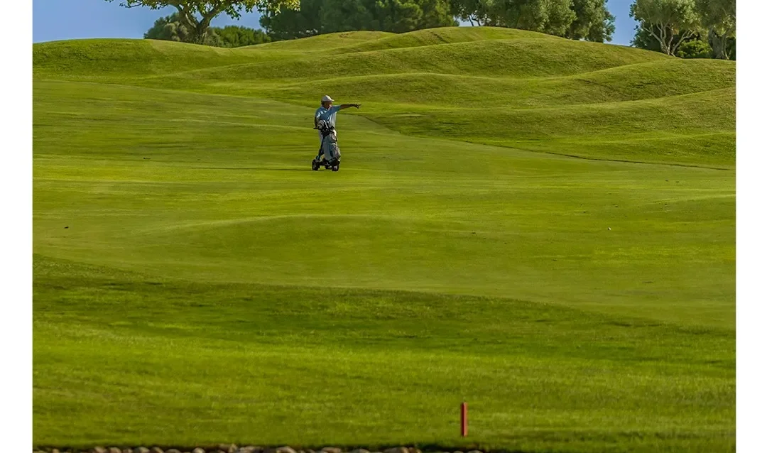golf-en-novo-sancti-petri-agosto-1 Jugador con carro recorriendo una amplia calle junto a un lago durante una jornada de golf en Novo Sancti Petri