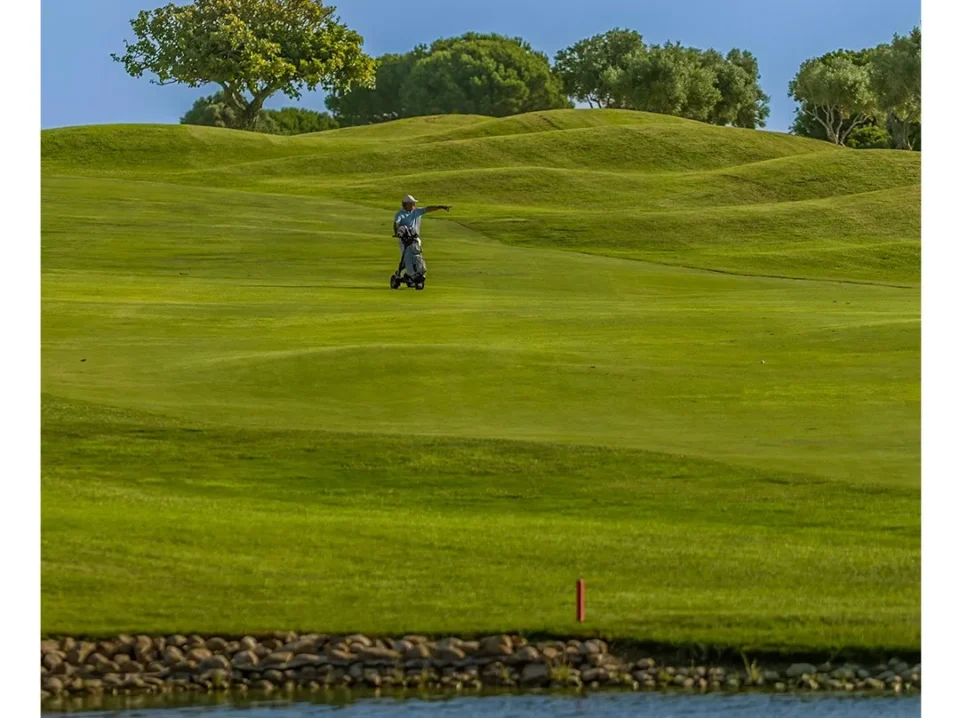 golf-en-novo-sancti-petri-agosto-1 Jugador con carro recorriendo una amplia calle junto a un lago durante una jornada de golf en Novo Sancti Petri