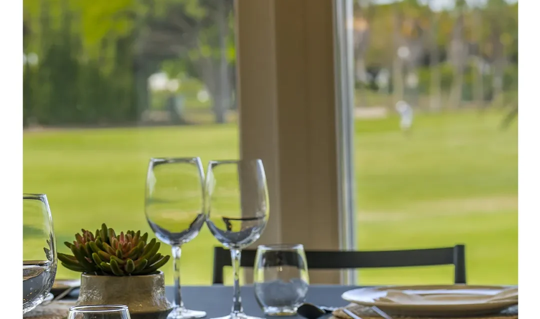 Mesa vestida junto al ventanal del restaurante con vistas a los fairways del Real Novo Sancti Petri, con pinar y palmeras al fondo